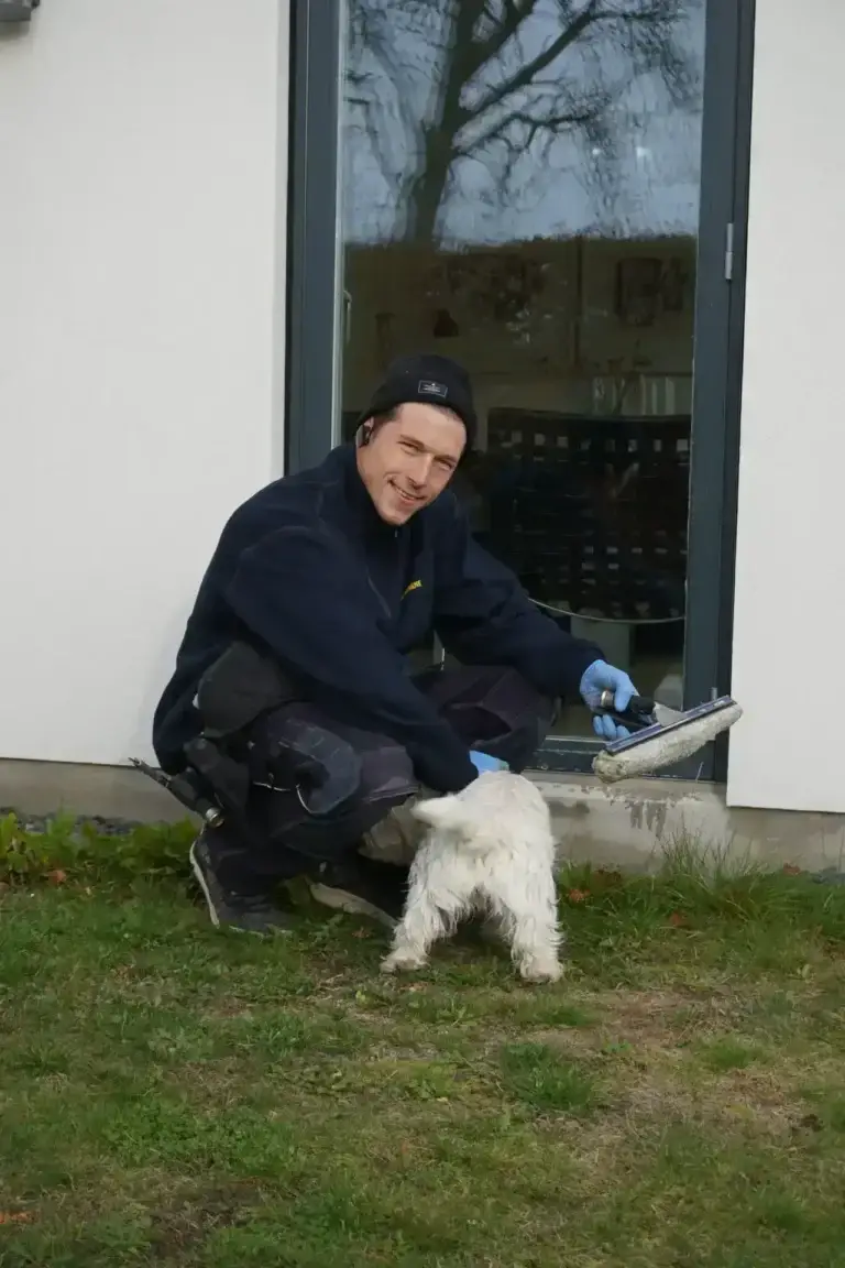 Vinduespudser bøjer sig ned for at klappe en hvid hund ved en rude